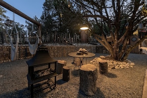 Zona esterna con posti a sedere, un tavolo e panche, circondata da alberi e un muro di pietra.