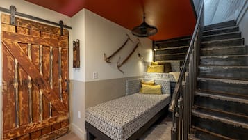 Un dormitorio con cama, una puerta de madera, una escalera y un ventilador.
