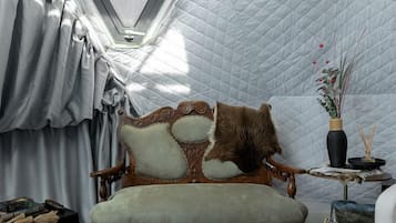 A room with a quilted ceiling, a vintage sofa, a small table with a vase, and a fur rug.