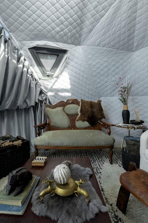 Una habitación con techo acolchado, un sofá antiguo, una mesita con un florero y una alfombra de piel.