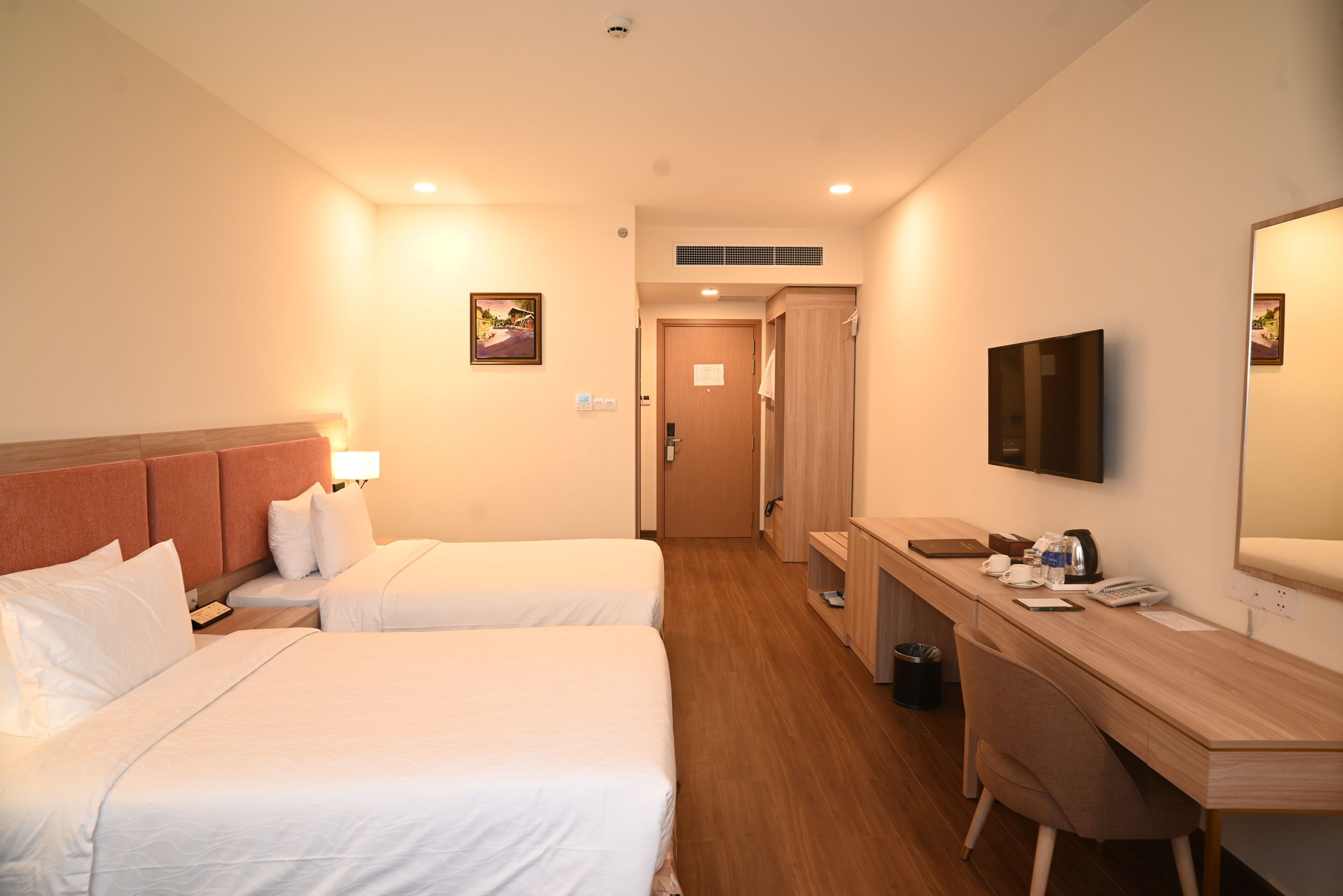 Ett hotellrum med två sängar, ett skrivbord, en stol, en tv och en dörr till badrummet.