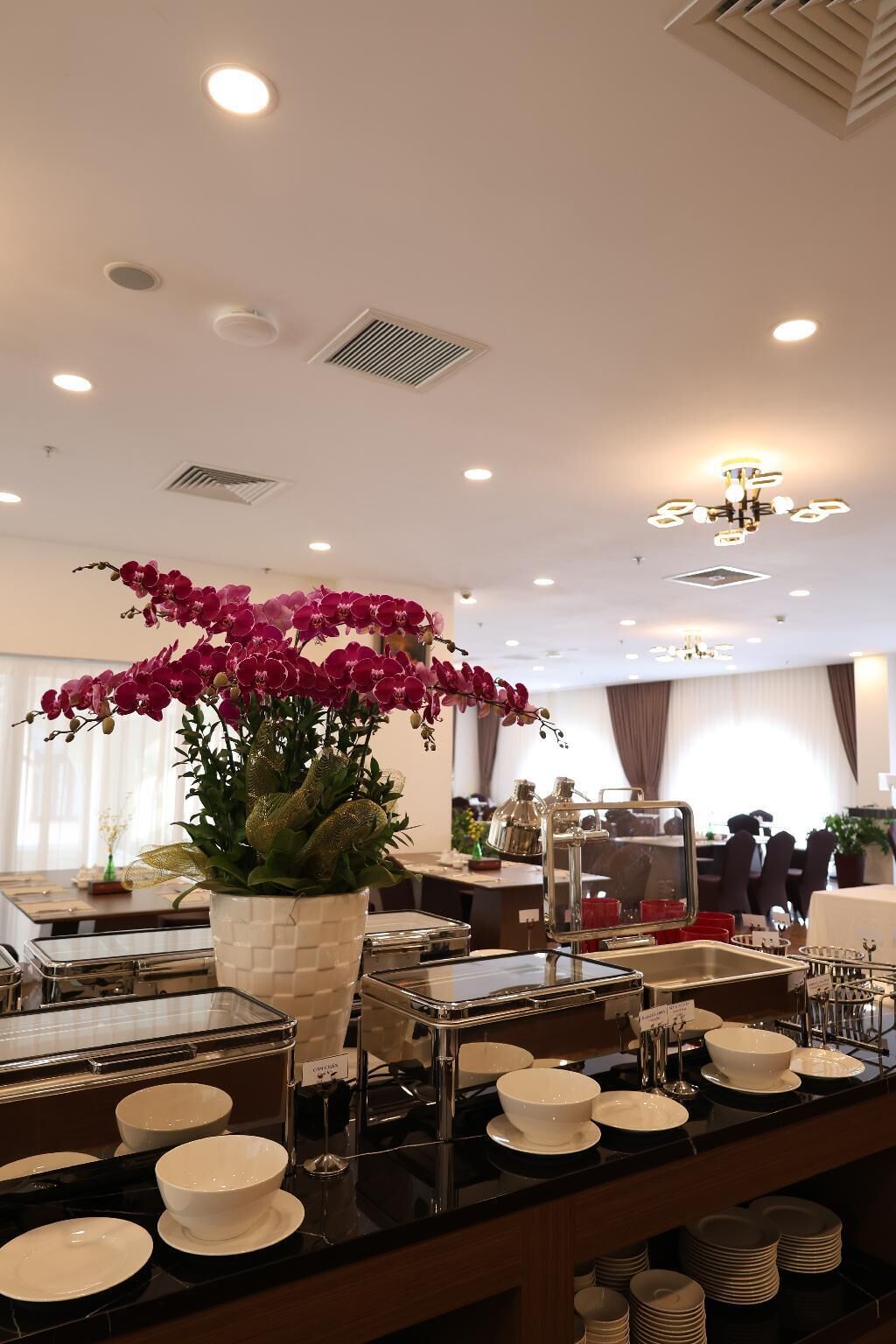 A hotel dining area with a buffet setup, a large orchid centerpiece, and a chandelier.
