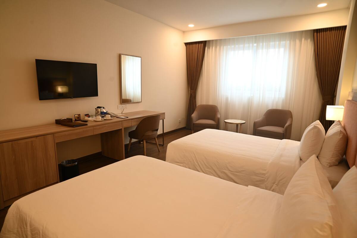 Une chambre d’hôtel avec deux lits, un bureau, une chaise, une télévision et une fenêtre avec des rideaux.