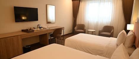 A hotel room with two beds, a desk, a chair, a TV, and a window with curtains.