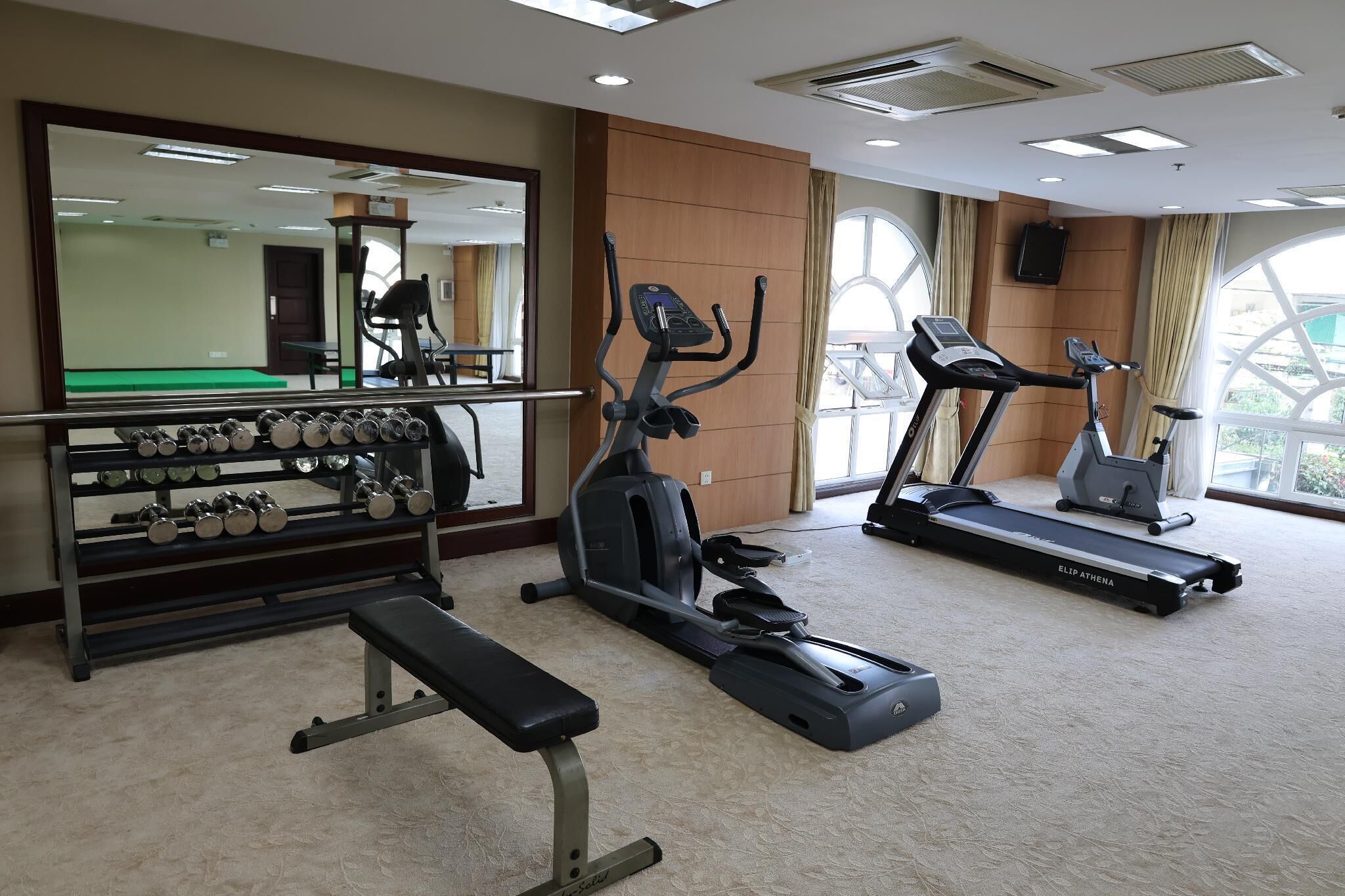 A gym with exercise equipment, a bench, and a mirrored wall.