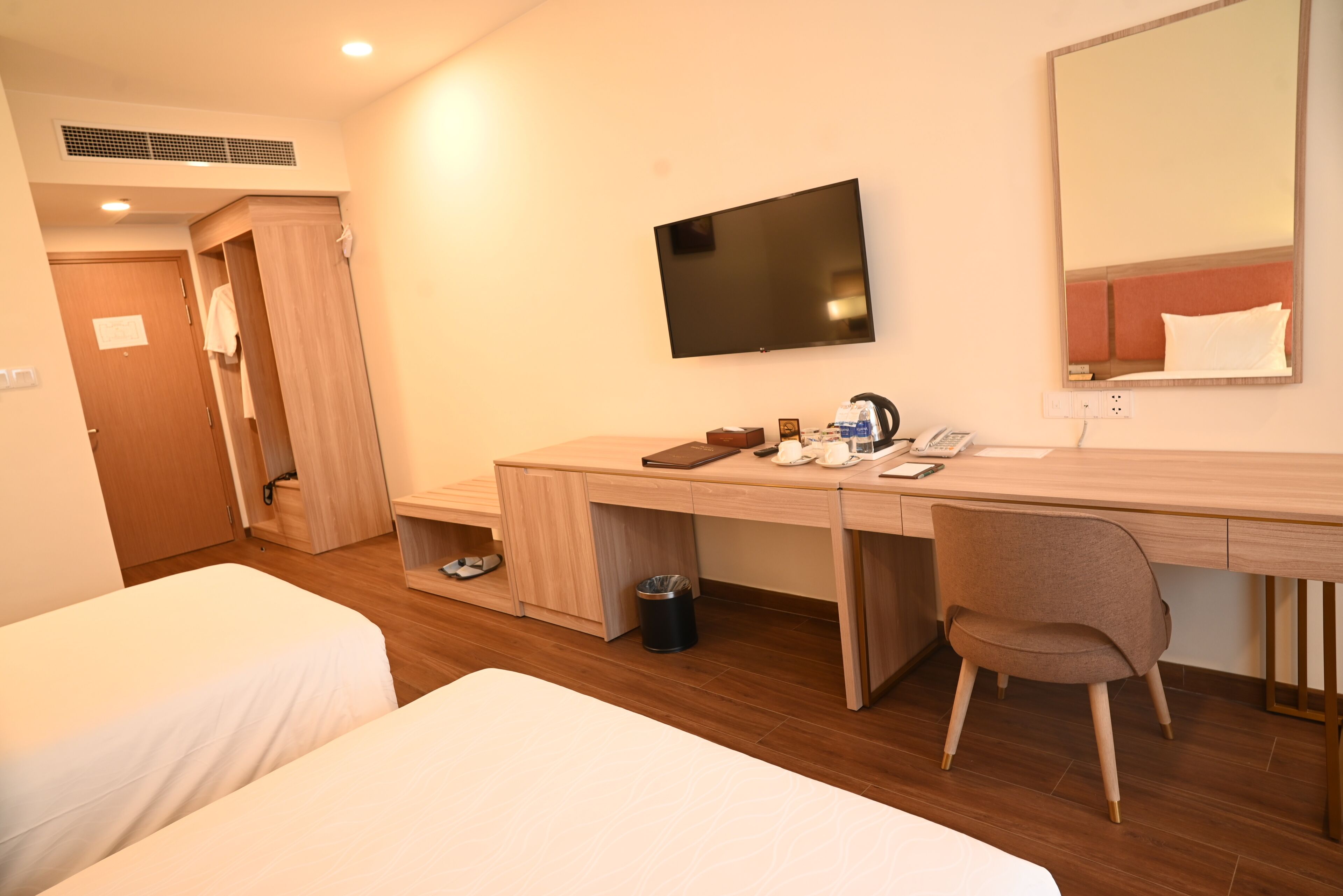 A hotel room with two beds, a desk with a chair, a TV, and a mirror.
