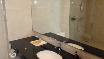 Une salle de bain moderne avec un grand miroir, un lavabo, une douche et des toilettes.