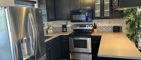 Una cocina moderna con electrodomésticos de acero inoxidable, armarios oscuros y un salpicadero decorativo.