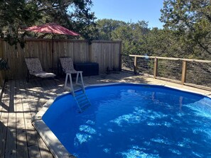A swimming pool with a wooden deck, a ladder, and two lounge chairs. - Wimberley Romance: Escape to a Cozy Cabin Nestled in Nature, TX (Wimberley)