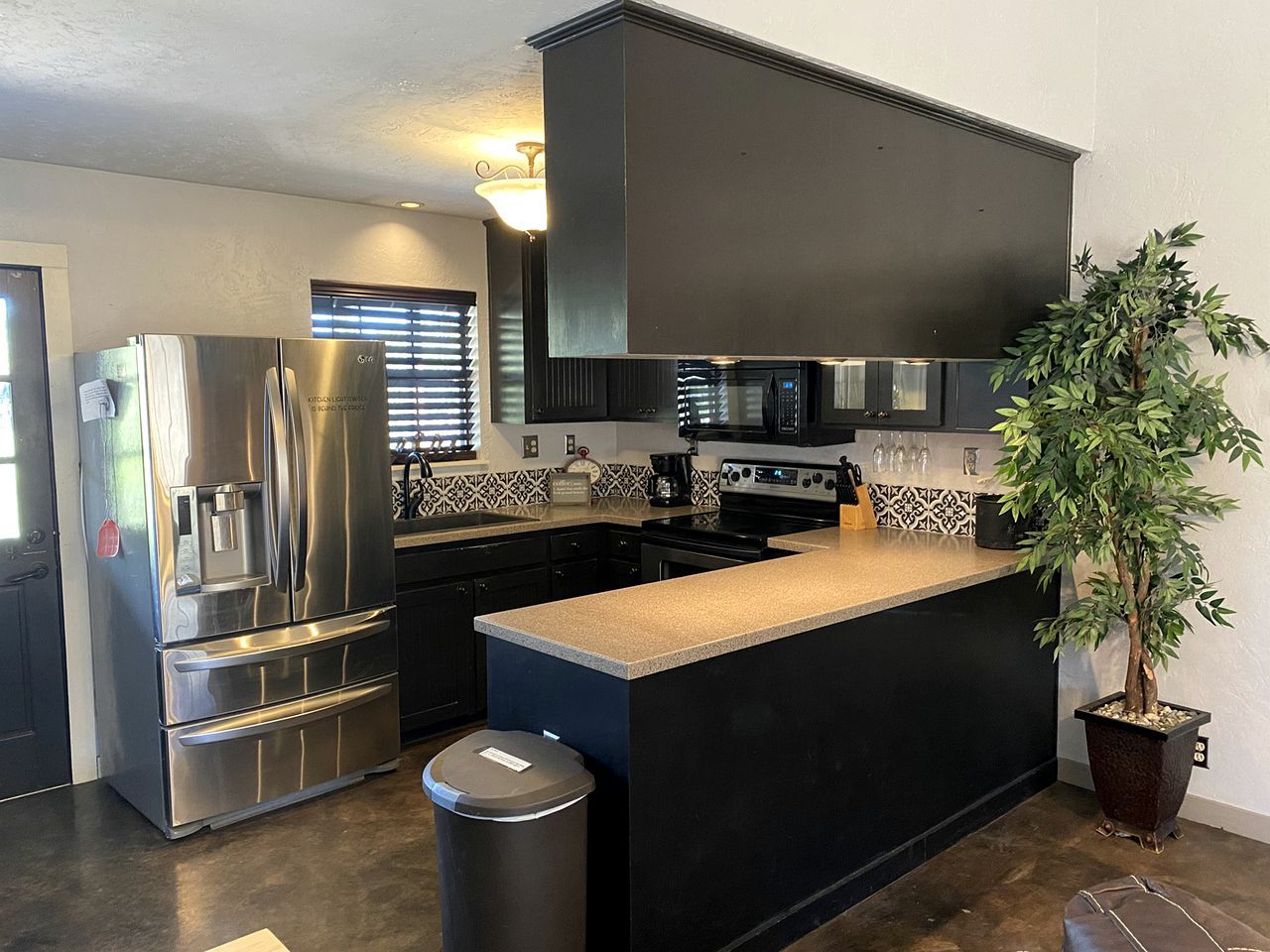 A modern kitchen with stainless steel appliances, a black countertop island, and a potted plant.
