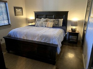 Een slaapkamer met een donker houten bed, een bed met een decoratieve spreideken, twee bedlampjes en een lijst met een afbeelding aan de muur.