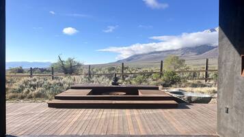 Una terraza de madera con un pozo de fuego y zona de estar, con vistas a un paisaje montañoso.