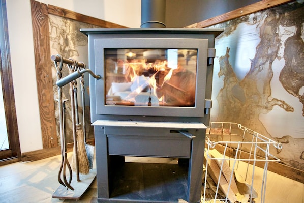 A wood-burning stove with a glass front, a metal stand, and a map on the wall behind it.