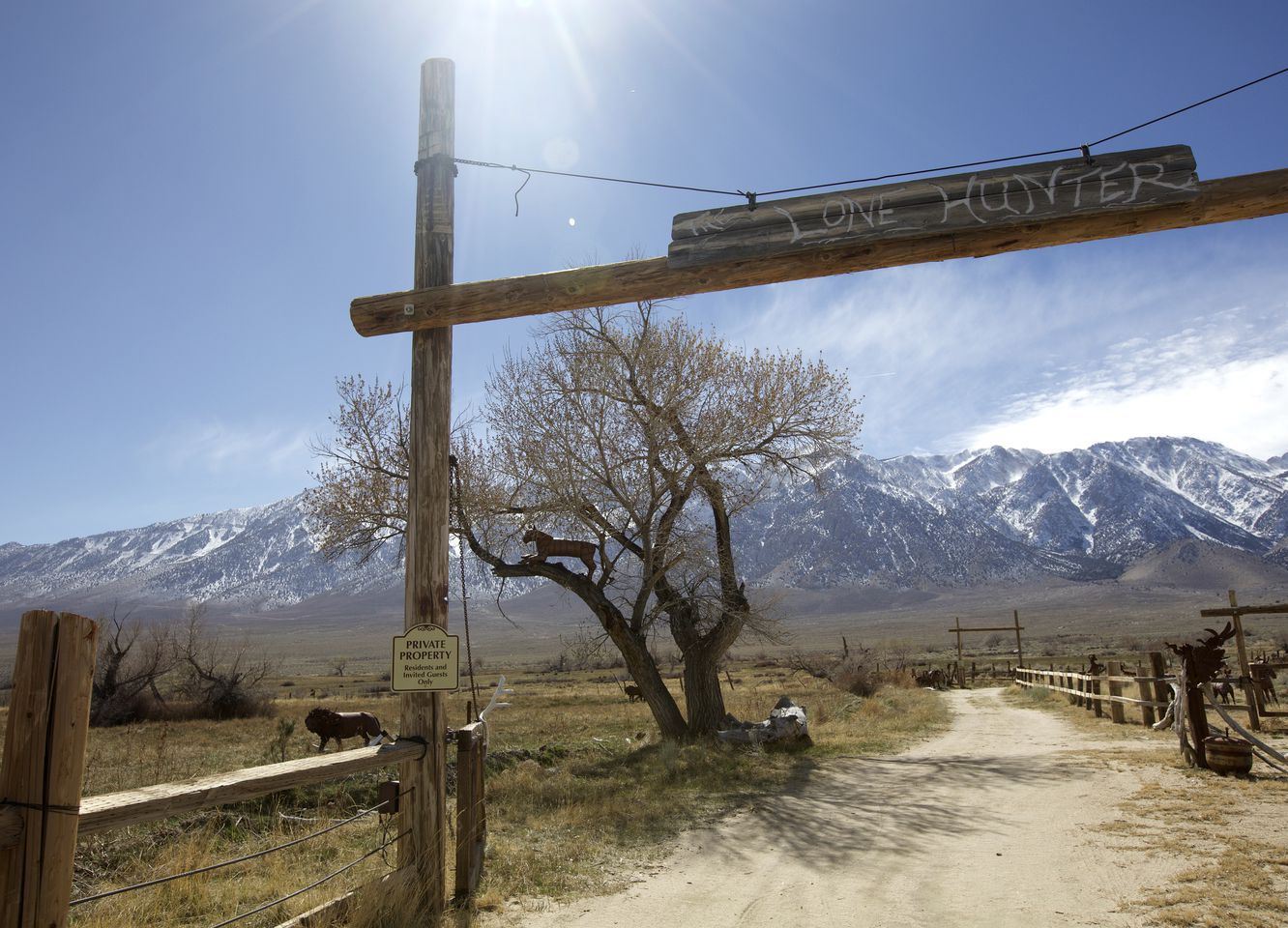A private property sign, a wooden gate, a dirt road, and a mountain range in the background.