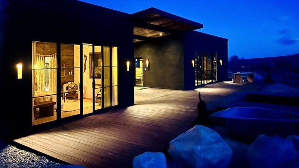A modern building with large glass windows, a wooden deck, and outdoor seating.