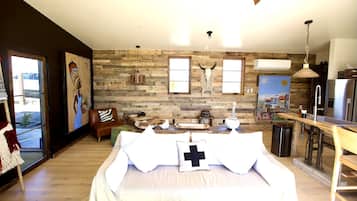 A bedroom with a large bed, a wooden wall, a dining area with a kitchen, and a window.