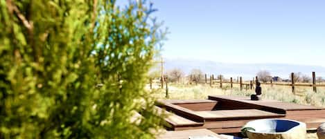 Une terrasse en bois avec un bassin en pierre et un banc en bois, le tout entouré d’une clôture et d’arbres.