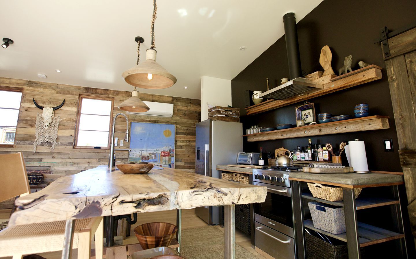 A modern kitchen with a rustic wooden wall, a large island, and built-in shelves.