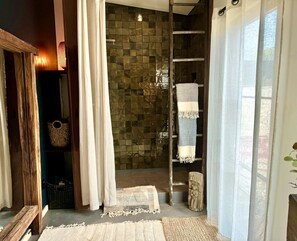 A bathroom with a shower, a towel rack, and a wooden bench.