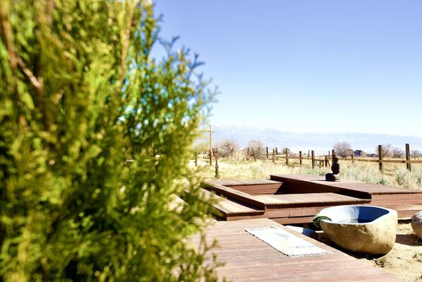A wooden deck with a stone basin and a wooden bench, surrounded by a fence and trees.