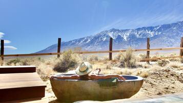 A wooden deck with a concrete bathtub and a hat on it, overlooking a desert landscape with mountains in the background.
