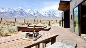 A wooden deck with a table, a bottle, and a mug, overlooking a mountainous landscape.