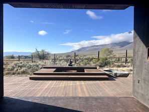 Un patio in legno con un braciere e un'area salotto, con vista su un paesaggio montuoso.