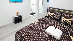 A hotel room with a bed, a TV, a clock, and a door leading to a balcony. - Swithome Properties Cozy Suite With Pond View, Near YEG Airport (Edmonton)