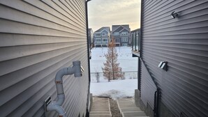 A pathway between two buildings with a metal pipe on the left and a gravel path on the right. - Swithome Properties Cozy Suite With Pond View, Near YEG Airport (Edmonton)