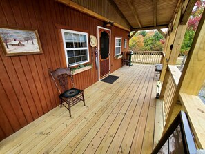 A wooden deck with a chair and a door, a painting on the wall, and a view of trees. - Wooden Rustic Cabin Great for Outdoor Activities in Liberty, Kentucky (Liberty)