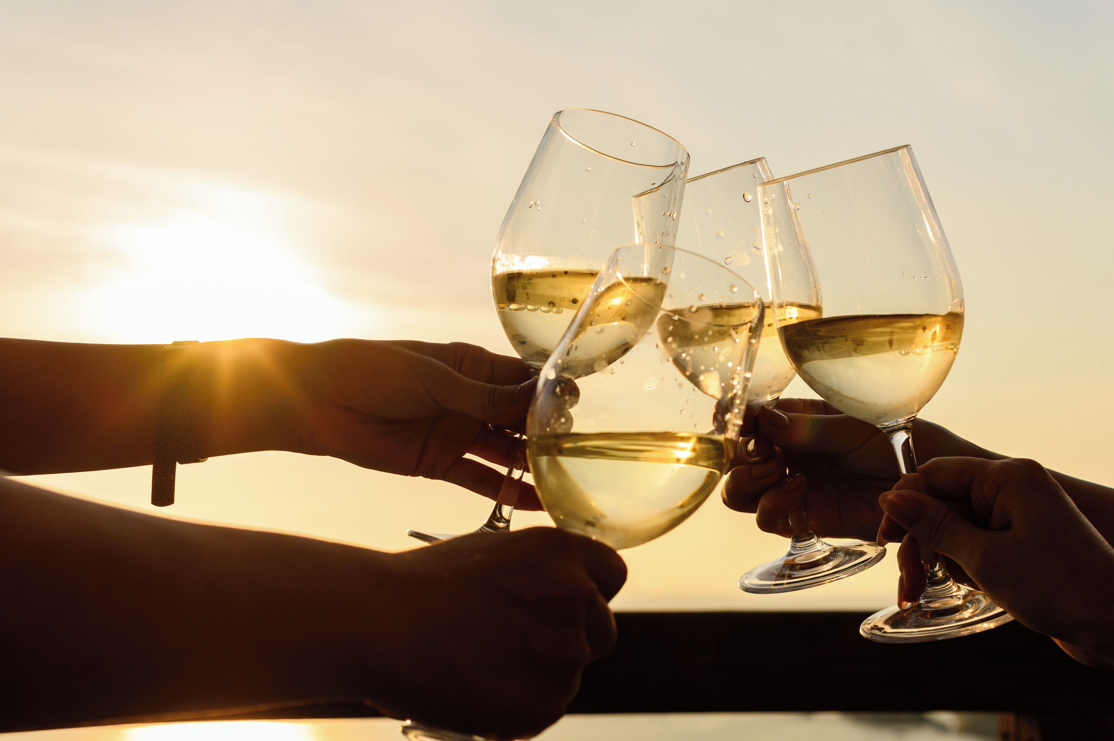 Three wine glasses held by hands against a sunset background.