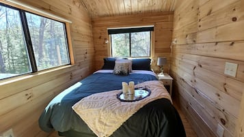 A wooden cabin bedroom with a bed, bedside table, and a window.