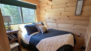 Une chambre confortable, aménagée dans un chalet en bois, avec un lit, une table de chevet, une fenêtre et une bibliothèque.