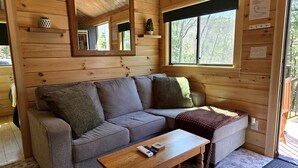 L’intérieur d’un chalet en bois, avec un canapé, une table basse, un miroir et une fenêtre.