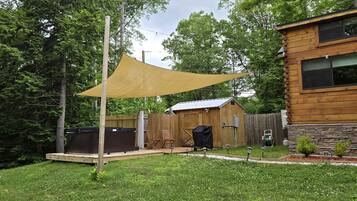 A backyard with a wooden deck, a barbecue grill, and a covered seating area.