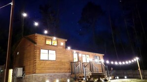 Une cabane en bois dotée d’un porche, illuminée par des guirlandes lumineuses et des lampadaires.