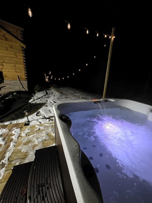A hot tub with a wooden deck and snow on the ground.