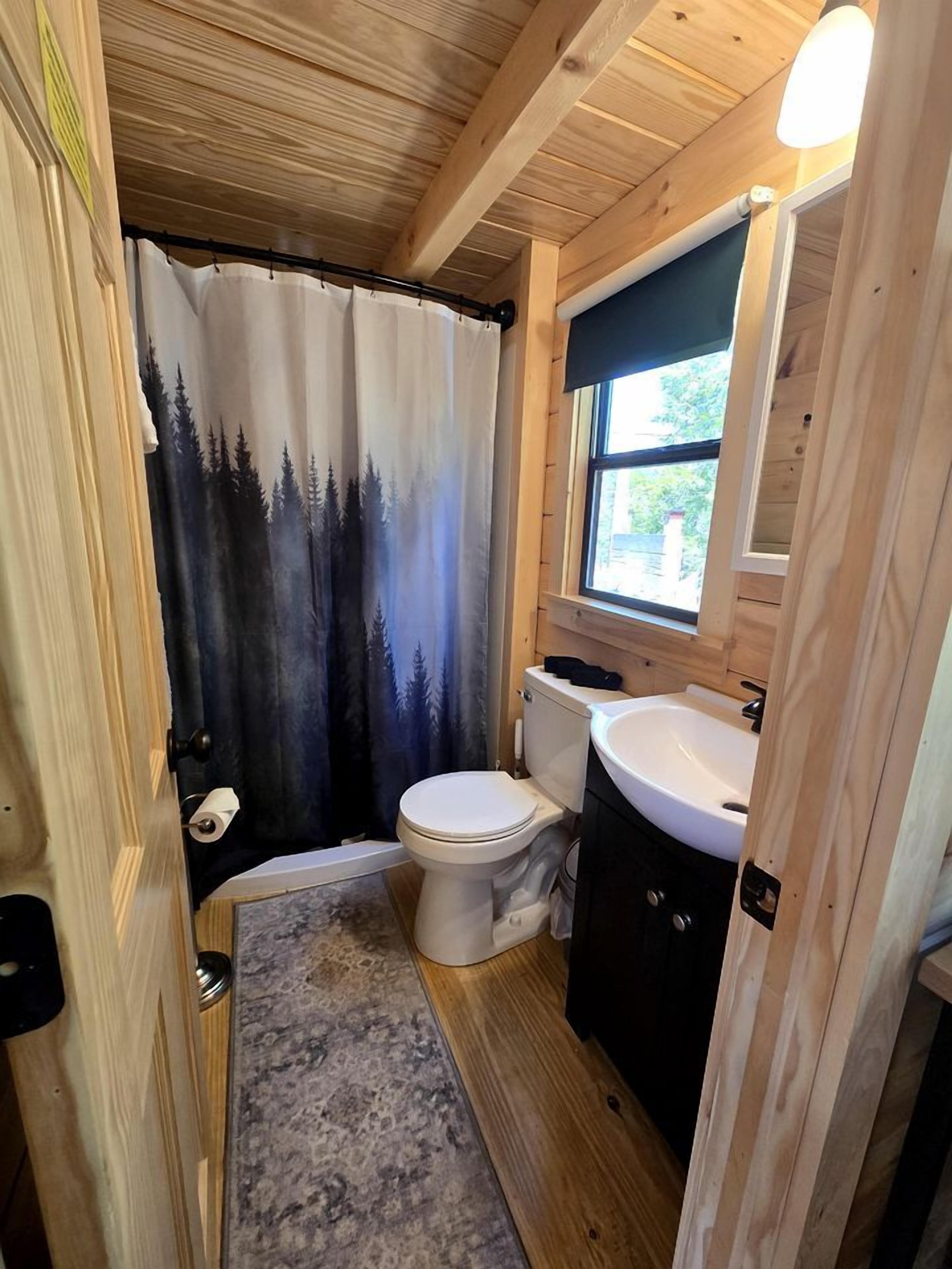 A compact bathroom with a toilet, sink, and shower curtain depicting a forest scene.