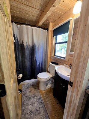 Ein kleines Badezimmer mit Toilette, Waschbecken und Duschvorhang mit Waldmotiv.