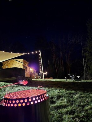 Una cabaña de madera con un espacio exterior cubierto, luces colgantes y una parrilla.