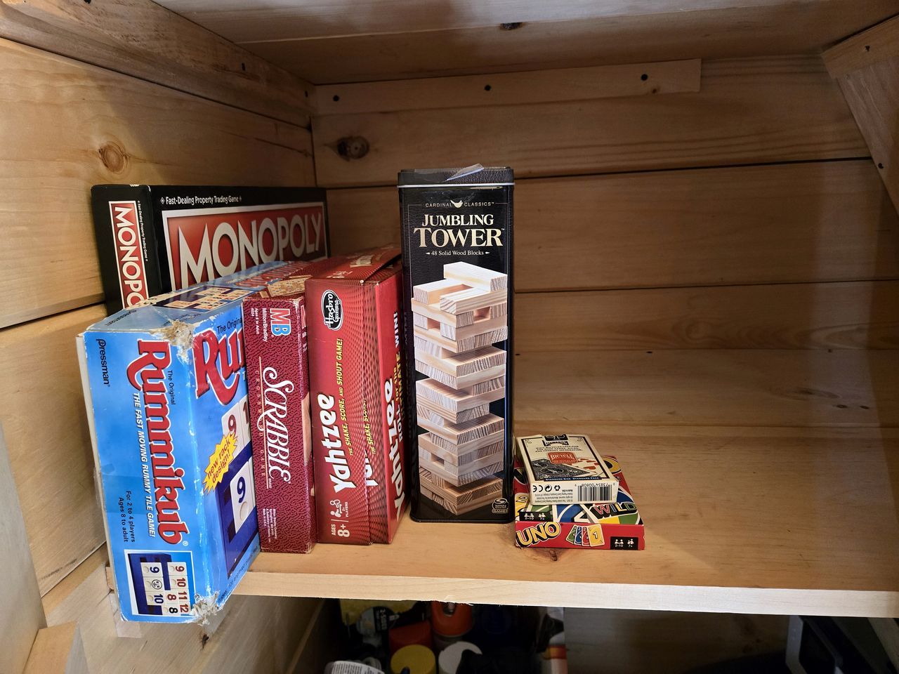 Una pràctica estanteria de fusta amb jocs de taula com ara Monopoly, Scrabble, Yahtzee, Jumble Tower i UNO.