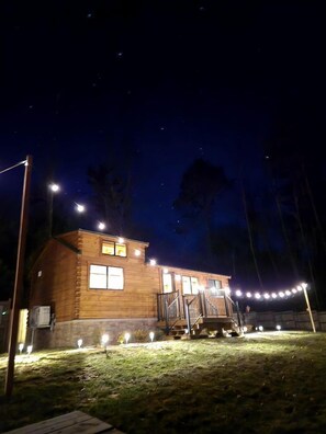 A wooden cabin with a porch, illuminated by string lights and street lamps.