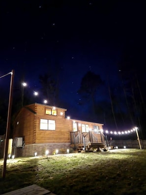 A wooden cabin with a porch, illuminated by string lights and street lamps. - Incredible Modern Tiny Log Cabin near the Ammonoosuc River for a Romantic Getaway in New Hampshire (Bath)