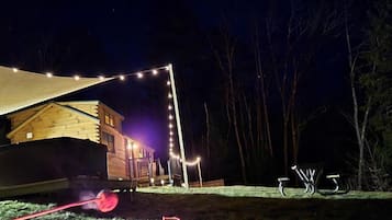 A wooden cabin with a covered outdoor area, string lights, and a grill.