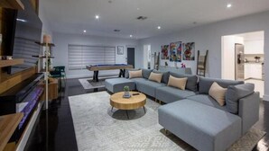 En moderne stue med en hjørnesofa, et billardbord og et fjernsyn.
