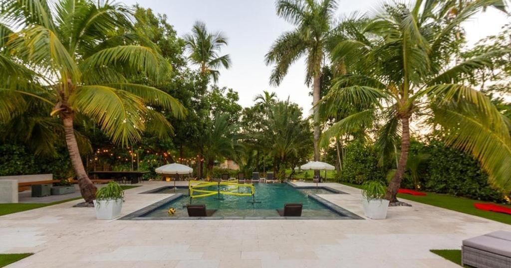 Piscina com palmeiras, espreguiçadeiras e um deck pavimentado.
