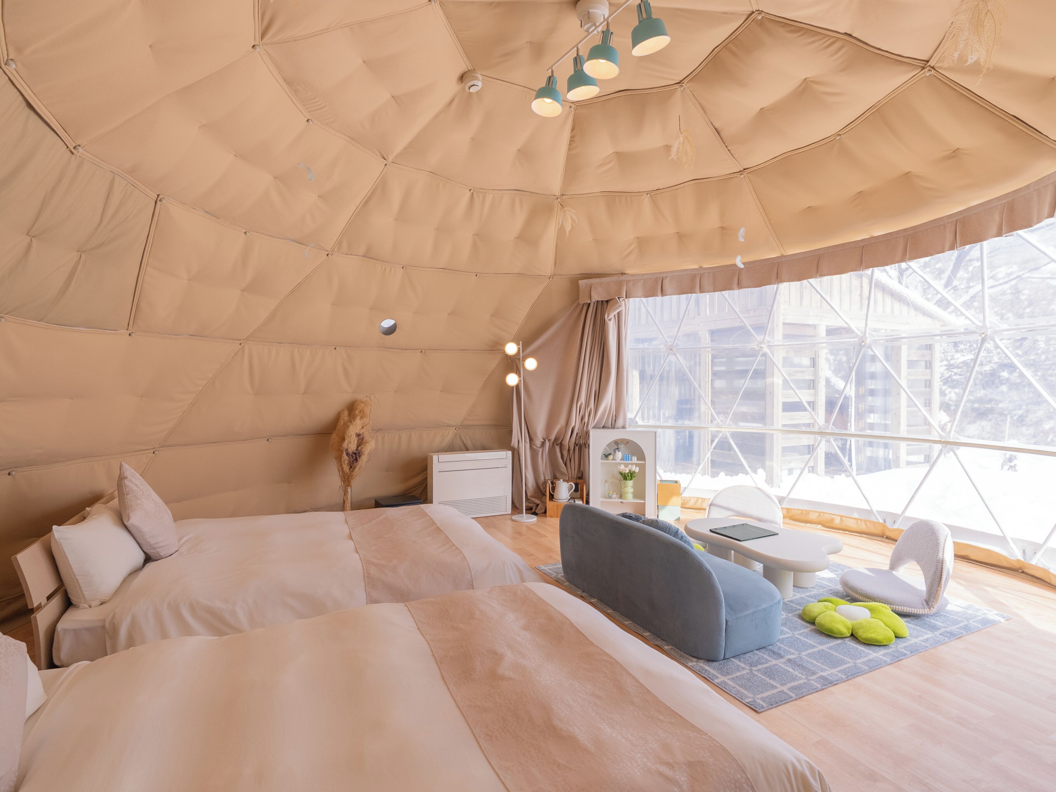 A cozy, well-lit tent-style room with a bed, seating area, and a window offering a view of the outside.