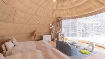 A cozy, well-lit tent-style room with a bed, seating area, and a window offering a view of the outside.