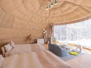 A cozy, well-lit tent-style room with a bed, seating area, and a window offering a view of the outside.