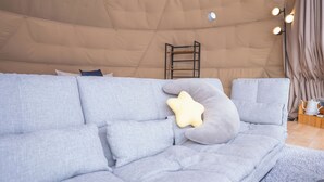 Alojamento tipo tenda com um sofá cinzento, almofadas em forma de estrela e uma escada encostada à parede.